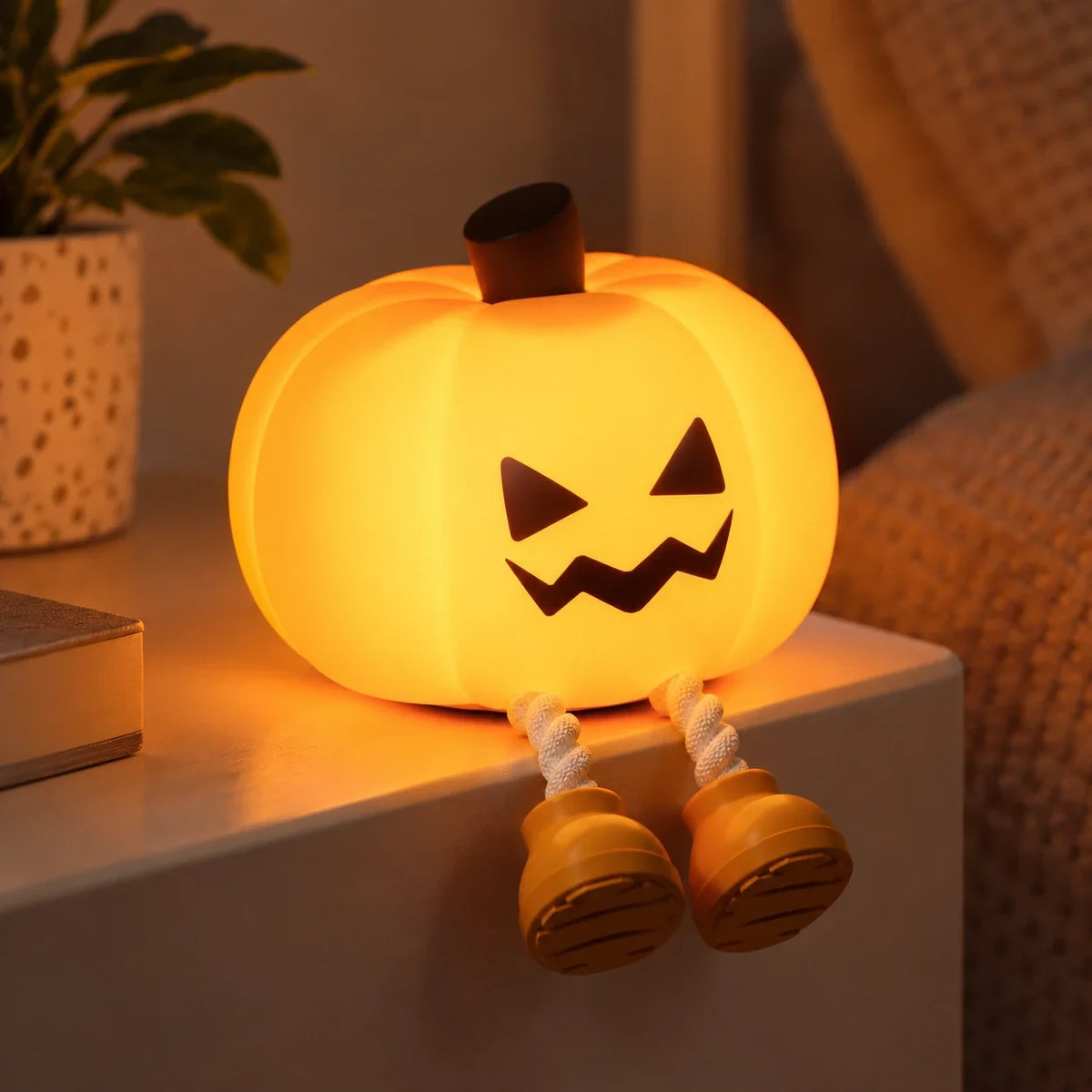 Silicone pumpkin lamp with the cheeky face, lit up next to some books